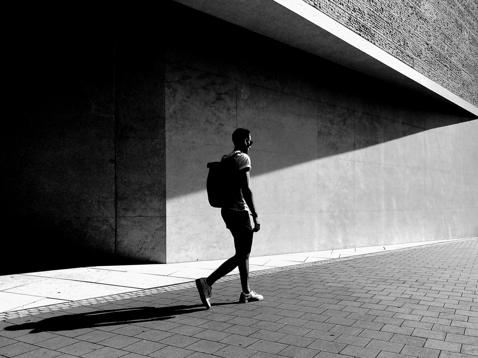 Walking man with a large diagonal shadow on a concrete wall.