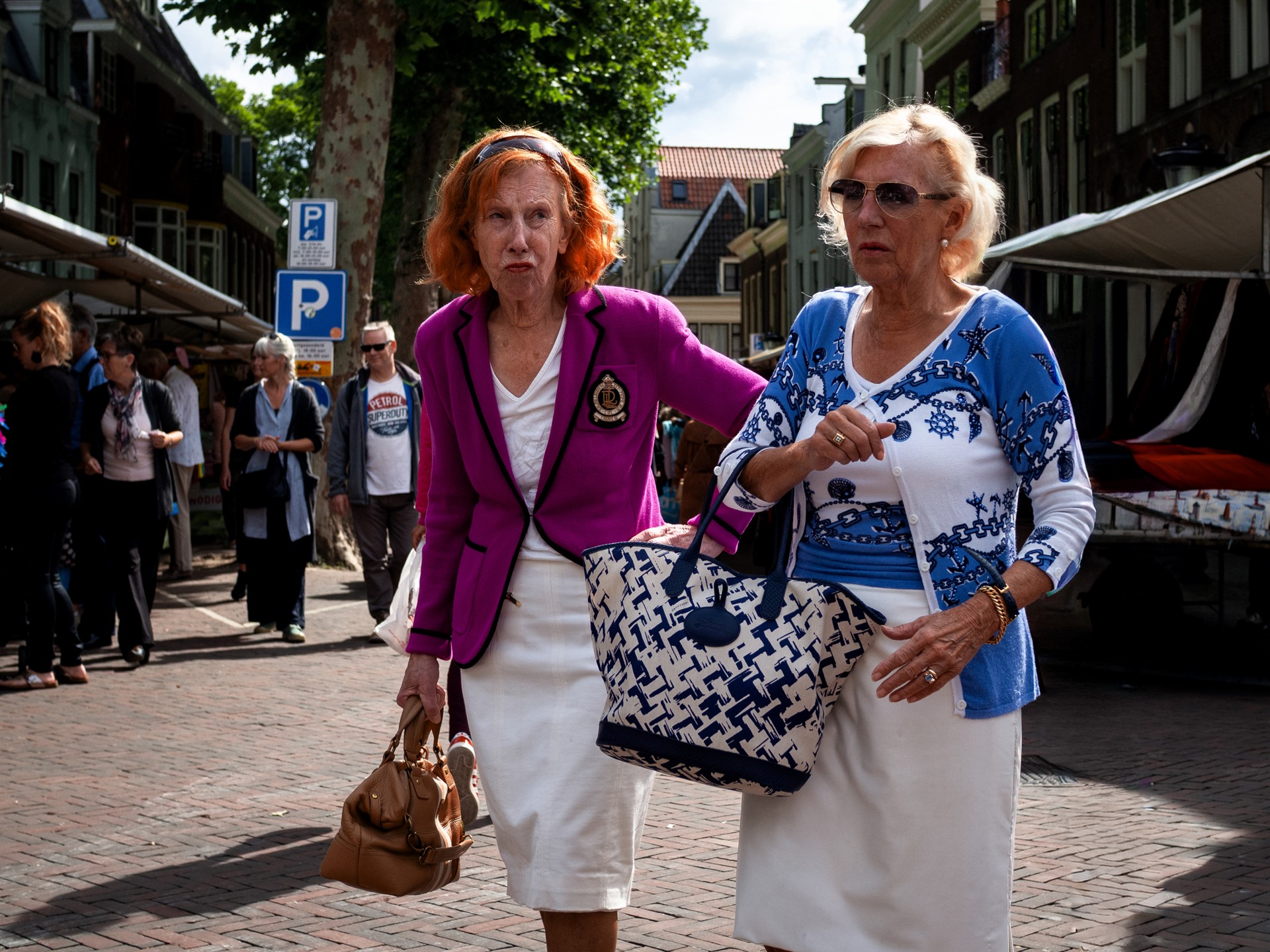 Two women in bright pink and blue clothing walking through a street market.
