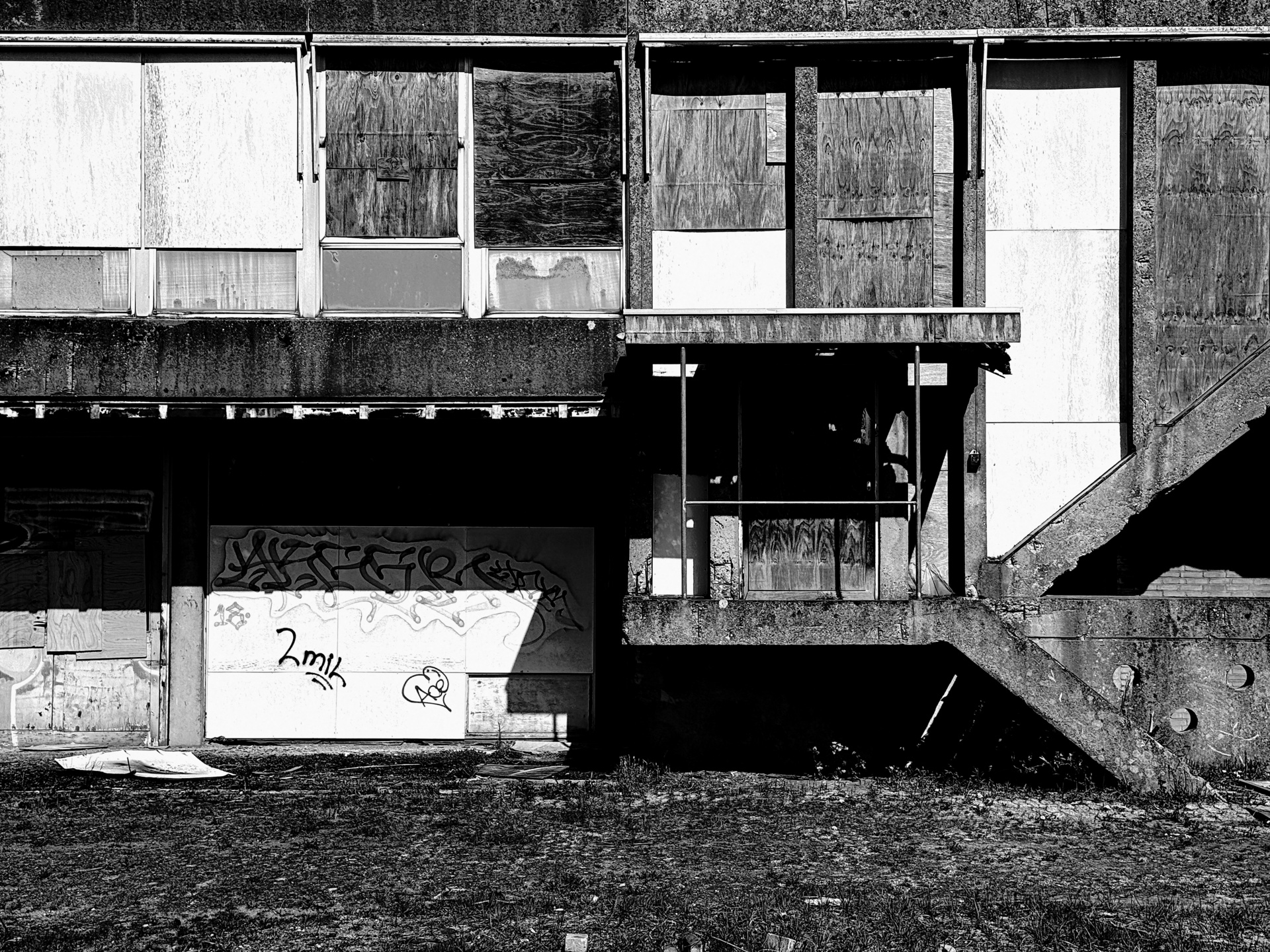 Boarded and weathered industrial facade with an exterior concrete staircase.
