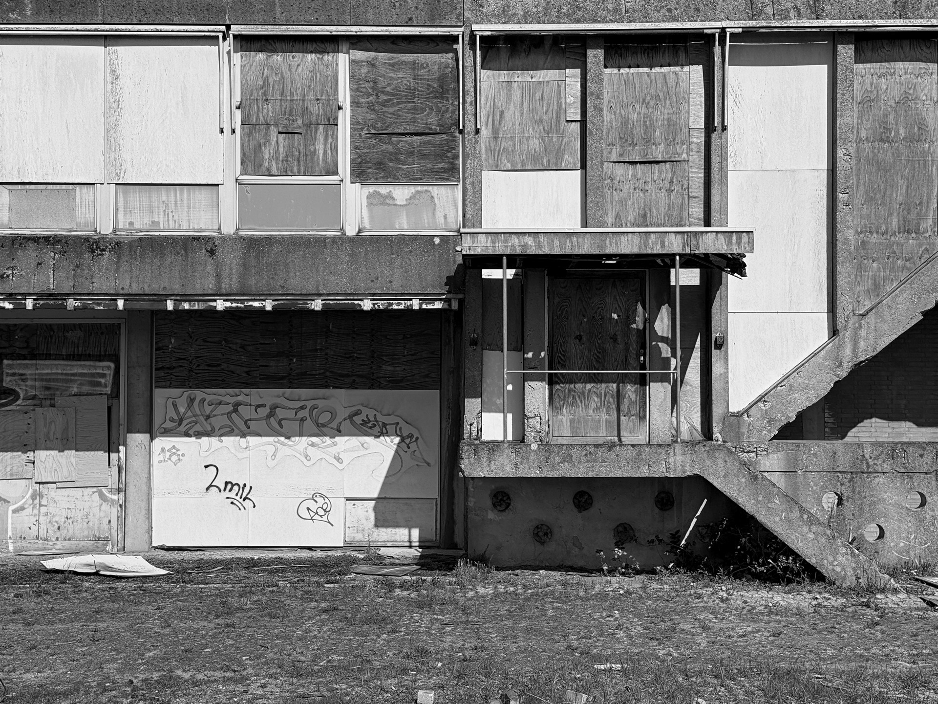 Boarded and weathered industrial facade with an exterior concrete staircase.